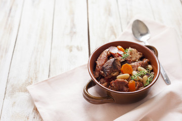 Cassoulet. Containing meat pork sausages, goose, duck and sometimes mutton and two types of white beans. French food. On old wooden white background.