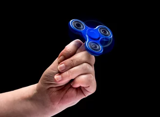 Foto auf Leinwand Spinning fidget spinnet toy in human left hand isolated on black background. Super popular device. © Leo Zank