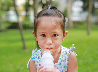 Closeup of little girl drinking milk with straw in the park. Portrait outdoor.