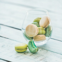 Colorful pastel pink, green and blue French macaron biscuits in glass over light blue painted rustic wooden table, copy space, square crop