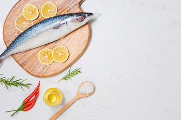 Fish dish cooking with various ingredients. Fresh raw fish decorated with lemon slices and herbs on wooden table.