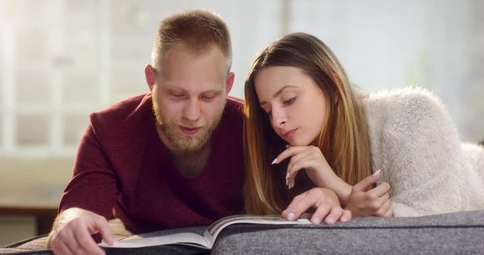 Young couple laying on couch and looking through a magazin