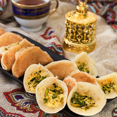 Traditional Arabic kataif pancakes stuffed cream and pistachios Prepared for iftar in Ramadan, oud in gold, on paisley background Square image