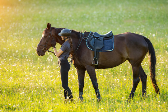 Young woman rider with her horse in evening sunset light