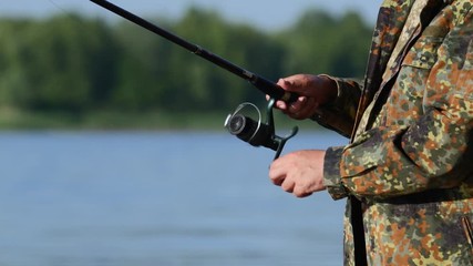 Fisherman's hands twist the coil on the handle, and pull out the fish