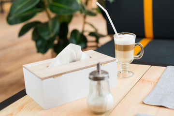 close up view of coffee latte, sugar and napkins on table in cafe