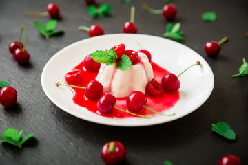 Tasty jelly with cherry berries in white plate on black table, traditional Italian dessert