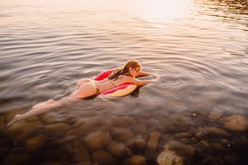 Beautiful woman swimming on donut in the sea at sunset. Slim lady relaxing on her holidays at ocean