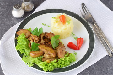 Fried bull testicles with cream and herbs served with mashed potato on a white plate on an abstract background. Healthy food concept