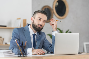 portrait of pensive businessman sitting at workplace with laptop in office