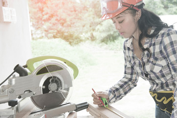 Pretty Asian carpenter woman is marking on wood for cut.