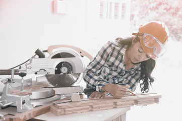 Pretty Asian carpenter woman is marking on wood for cut.