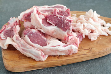 Raw lamb chops and fat on a olive wood cutting board on a grey abstract background. Healthy cooking concept