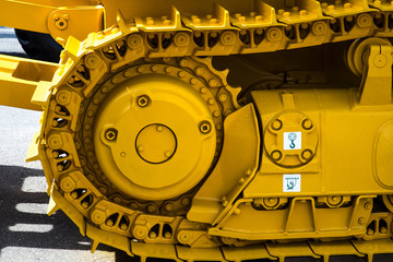 Bulldozer tracks and drive gear with sprocket mechanism, large construction machine with bolts and yellow paint coating, heavy industry, detail