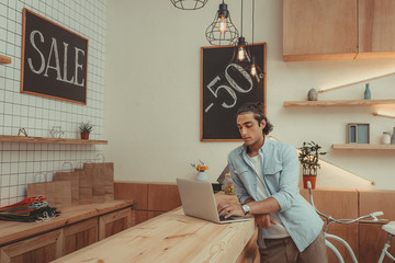 concentrated young shop owner using laptop while working indoors