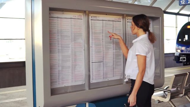 Young businesswoman checking departure timetable board  in the railway station stop
