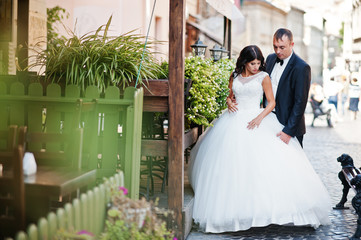 Amazing young attractive newly married couple walking and posing in the downtown with beautiful architecture and flowers on the background on their wedding day.