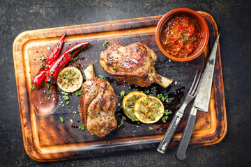 Barbecue Lammhaxen mit Tomaten Chili Relish als Draufsicht auf verbranntem Schneidebrett