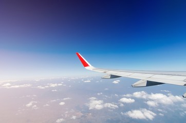 Fototapeta na wymiar airplane wing flying in blue sky and cloud with view of earth from height from window, sunlight effect, travel and transportation concept