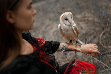 Girl sits on grass with owl on her hand in forest. Close-up.