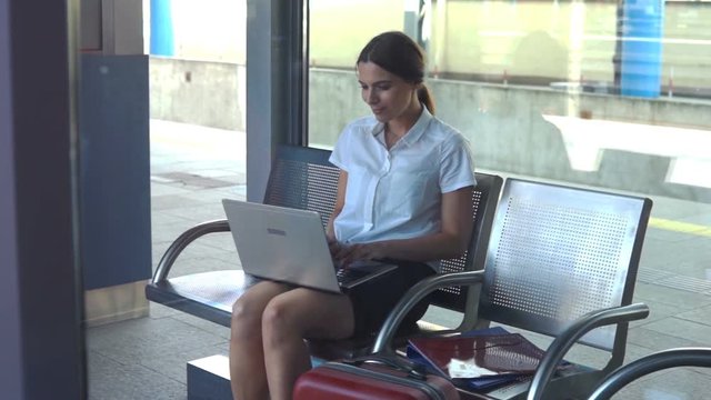 Young businesswoman working on laptop sitting in the railway station
