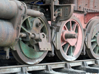Old wrecked steam locomotive on tracks with rust fading green and red paint and missing parts