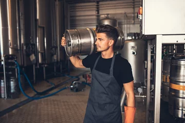 Crédence de cuisine en verre imprimé Bar Young male brewer carrying keg at brewery