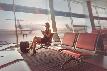 Happy charming lady is sitting on bench at airport - obrazy, fototapety, plakaty
