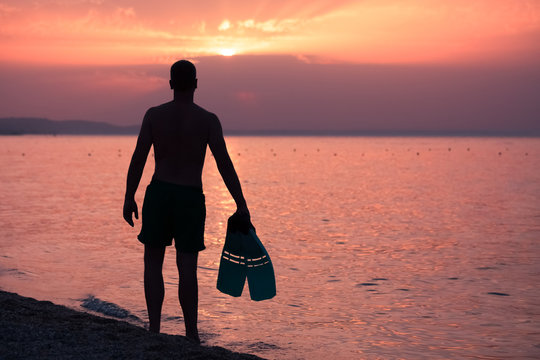 Man holding snorkel fins on beach at sunset