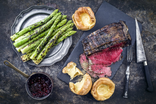 Barbecue dry aged rib of beef with green asparagus and yorkshire pudding as close-up on an old metal sheet