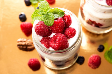 Healthy breakfast - dessert with yogurt, granola, outs flakes, jam, raspberries, blueberries, hazelnut and mint in yogurt jars on gold background. Concept for healthy eating or breakfast.Top view. 