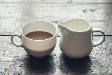 White cup of coffee with milk and jug on wooden rustic table