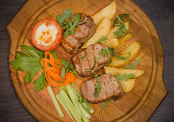 Three pork steaks with fried potatoes and vegetables on a wooden background