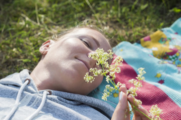 Obraz premium A young girl lies on the field and sniffs a flower