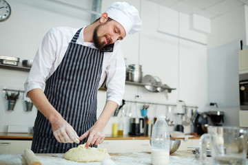 Chef in uniform talking by cellphone while kneading dough