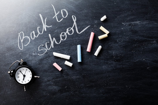 Back to school background on blackboard with colorful chalks and alarm clock.
