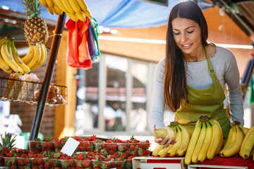 Obraz premium Young attractive fruit market saleswoman sells fresh fruit on the street market.