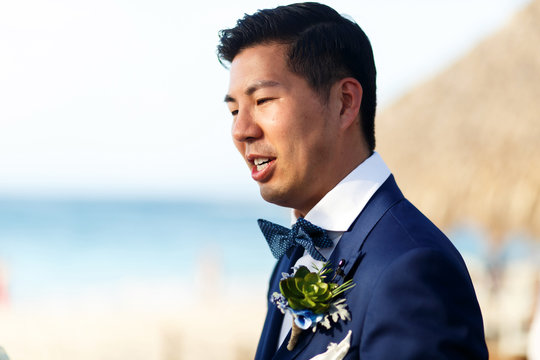 Asian groom in blue suit stands on the beach