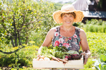 Senior woman holding wooden crate with vegetables in the garden