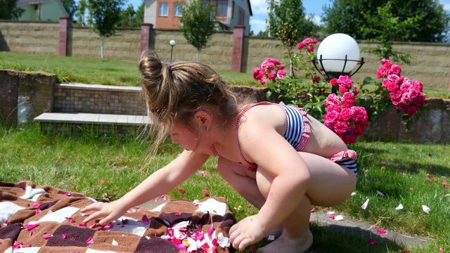 Little girl collects rose petals in the garden.