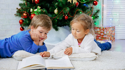Two cute childes lying on the floor and reading book at christmas eve.
