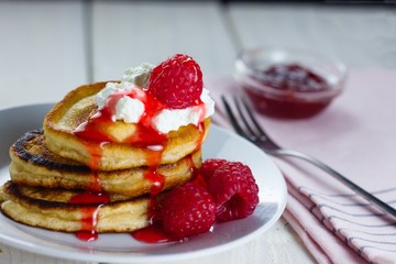 Pile of pancakes with fresh raspberries and a little whipped cream dripping red berry sauce