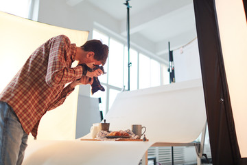 Young photographer shooting food composition on table in production studio