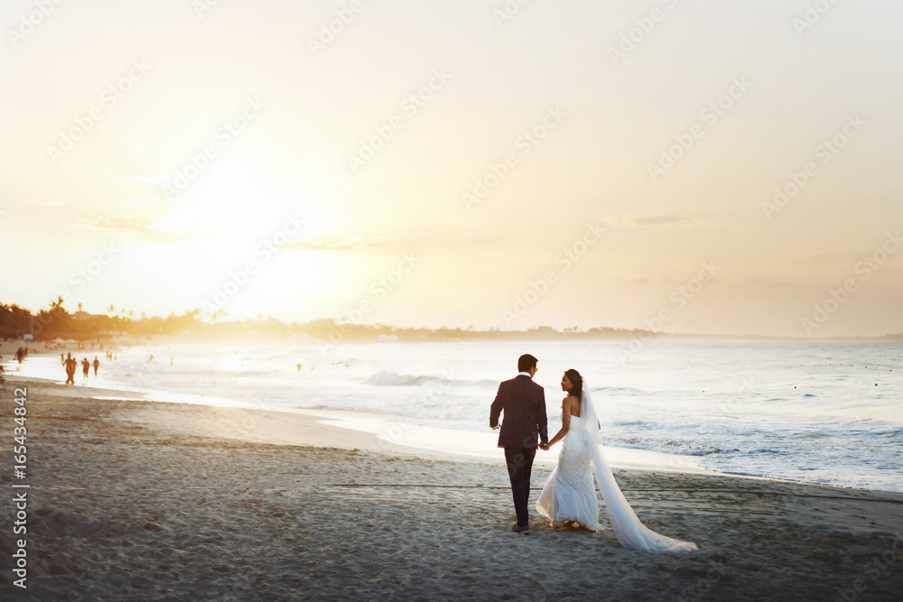 Wall mural bride and groom hold each other hands posing on the beach