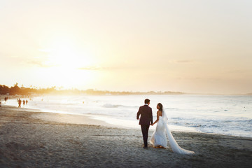 Bride and groom hold each other hands posing on the beach