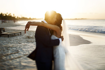 Bride and groom hug each other tender standing in the rays of golden sun on the beach