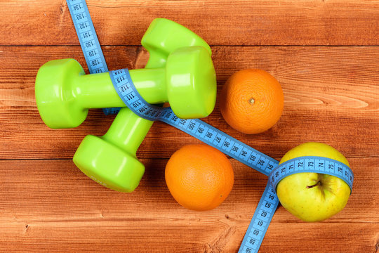 fitness concept, dumbbells weight with measuring tape, orange and apple