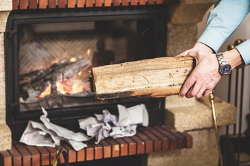 Hands of man holding piece of wood in front fireplace