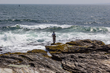 Fisherman on rocks looking out to the wave in Beavertail Rhode Island
