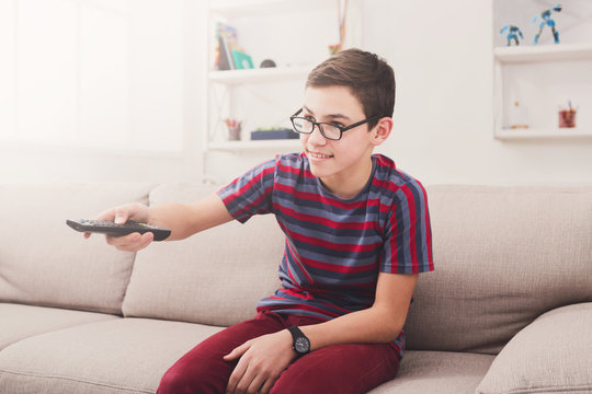 Teenager boy watching television, using TV remote controller